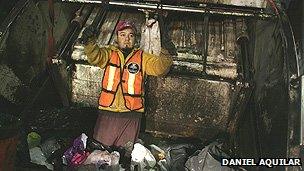 A rubbish collector stands inside the truck