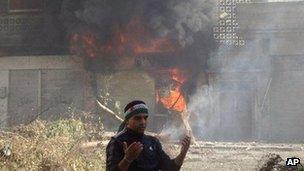 A protestor gestures in front of a shop damaged by shelling by Syrian government forces. Image provided by the opposition Local Coordination Committees