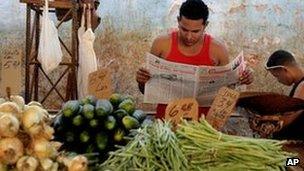 Suliban Molina, centre, reads state-run newspaper Granma as he waits for customers at a food market in Havana, Cuba, 27 January 2012