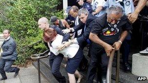 Australian Prime Minister Julia Gillard is bundled out of a restaurant by security service agents after it was surrounded by Aboriginal rights protesters in Canberra on 26 January, 2012