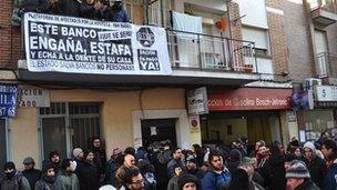 Protesters fill a Madrid street beneath a balcony displaying a banner