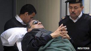 Former Egyptian president Hosni Mubarak lies on a gurney bed while leaving the Cairo courtroom where he is on trial