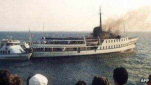 Bystanders watch the City of Poros cruise ship burning after the 1988 attack