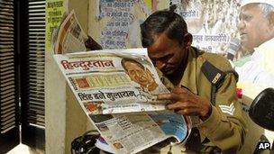 An Indian man reads a newspaper in front of torn posters depicting Mahatma Gandhi, left, and anti-corruption activist Anna Hazare, in Lucknow, India, Wednesday, March 7, 2012. India's governing Congress party was badly beaten in a key state election .