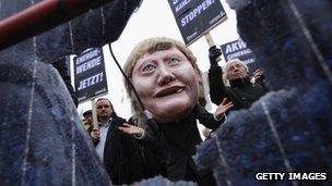 Protesters with an effigy of Mrs Merkel looking through a torn solar panel