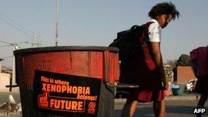 A picture taken on August 12, 2009 shows South African school girls walking past a trash bin bearing an a sticker against xenophobia in Alexandra township, north of Johannesburg