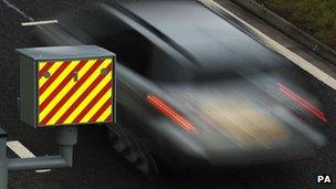 A sharp picture of a speed camera box with a blurry image of a car speeding past.