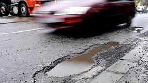 A car drives past a pothole