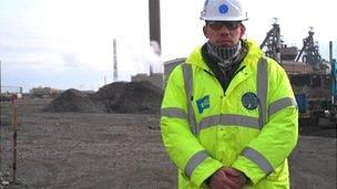 A picture of Kerry Jones in a high-vis jacket and hard hat standing in front of a work site.