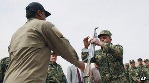 A former private security guard (left) hands over his weapon to Jamal Abdul Naser Sidiqi, head of the Afghan Public Protection Force