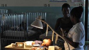 A toddler in hospital is tended by two women, Bong County, Liberia, 9 April 2012