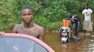 Man leans on car door next to river, Gbarnga, Liberia, 9 April 2012