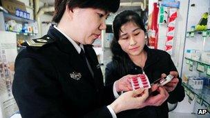 An official from local Food and Drug Administration, left, checks out capsule medicine in a drug store in Qingdao in east China's Shandong province, 16 April 2012
