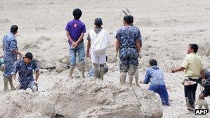 Police and military personnel, aided by civilian volunteers, dig through mud and silt during rescue operations