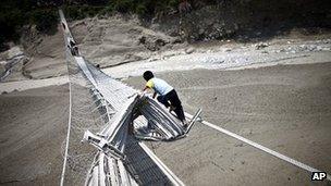 Nepalese villagers try to cross the Seti river through a damaged suspension bridge at Kharapani village, in the western Kaski district of Nepal (6 May 2012)