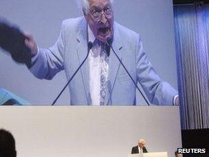 An unidentified shareholder is seen on a huge screen as he holds up his shoe while Swiss bank Credit Suisse