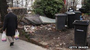 Pedestrian walks past rubbish in someone's front garden