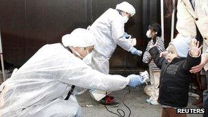 Officials in protective gear check for signs of radiation on children who are from the evacuation area near the Fukushima Daiichi nuclear plant in Koriyama, March 13, 2011.