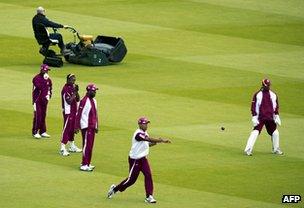 Groundsman at Lords cricket ground tends the grass as west Indies players warm up for a match