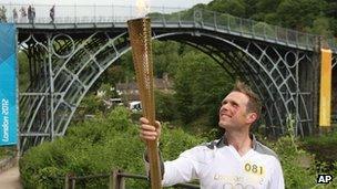 Torchbearer Lyndon Flavell holding the Olympic flame next to the Iron Bridge at Ironbridge Gorge