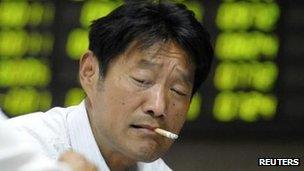 An investor smokes in front of an electronic board showing stock information at a brokerage house in Nanjing, Jiangsu, 9 May 2012