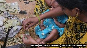 Baby in lap of mother as she rolls beedis