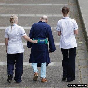 Two NHS staff walk with an elderly patient