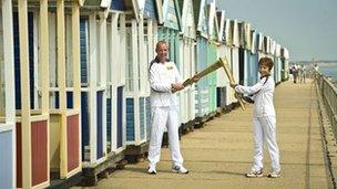 Richard Game passes the flame to Torchbearer Caroline Emeny in front of the Southwold beach huts