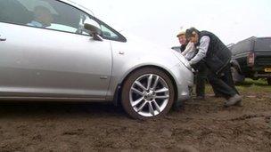 Two people pushing a car in a muddy field