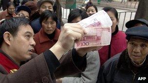 A bank employee shows customers on the street discrepancies between a real and a fake 100 Renminbi note.