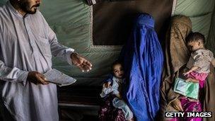 are held by their mothers wait to receive their polio vaccination in the Merlin clinic at the Jalozai UNHCR Camp for