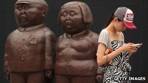 A Chinese woman uses a mobile in front of two statues in Beijing