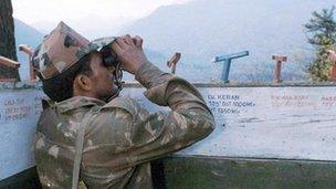 An Indian army soldier monitors Pakistani troop movements with binoculars in a bunker near Keran