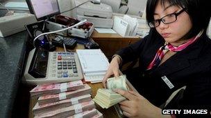 A bank teller counting stacks of US dollars and Chinese 100-yuan notes at a bank in Hefei, east China's Anhui province.