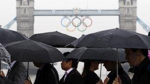 Commuters walk across London Bridge, as Tower Bridge adorned with the Olympic rings