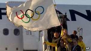 Rio de Janeiro's Mayor Eduardo Paes, top left, Carlos Arthur Nuzman, President of the Brazilian Olympic Committee, bottom right, and Brazilian athletes hold the Olympic flag on its arrival in Rio de Janeiro, Brazil