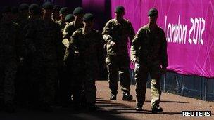 Soldiers patrol past signage for the London 2012 Olympic Games near the beach volleyball courts at Horse Guards Parade in London