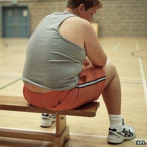 An overweight boy sits on a gym bench