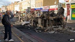 A passer-by takes a photo of the remains of a double decker bus.