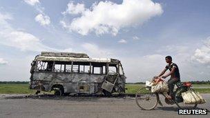 A man rides a bicycle in front of a bus that was burnt by a mob on the national highway near Rongia town in the northeastern Indian state of Assam in this August 16, 2012 file photo