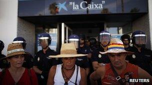 Members of the Andalusian Union of Workers (SAT) protest in front of Spanish riot police as they guard the entrance of a Caixa bank branch