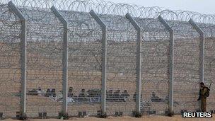 Soldier and a group of African migrants near the border fence between Israel and Egypt