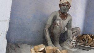 Worker Narayanswamy with polythene covering his head hammering explosive powder into cones with body covered in aluminium powder