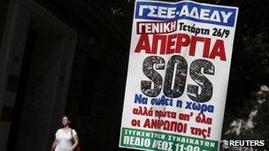 A woman walks next to a banner calling for a 24-hour general strike against austerity measures in Athens (25 Sept 2012)