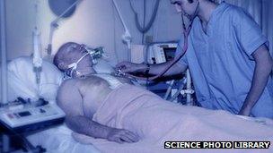 Member of medical staff using a stethoscope to listen to the chest of a male patient in an intensive care unit