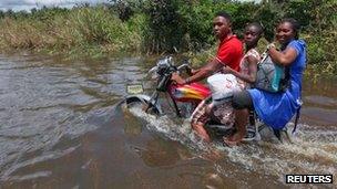 A man rides a motorcycle with passengers along a flooded road in the Patani community in Nigeria's Delta state - 15 October 2012