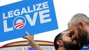 Two men campaigning in favour of same-sex marriage kiss in front of a Legalize Love placard