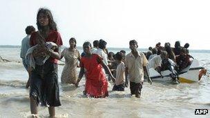 A Tamil mother holding her baby walks ashore after fleeing the conflict in 2009 by boat