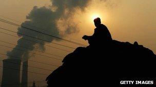 A sits near a power plant emitting plumes of smoke in Beijing, China. File photo