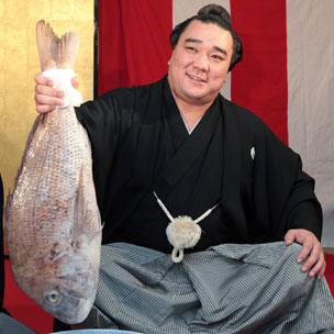 Mongolian sumo wrestler Harumafuji holds a large red sea bream and smiles after he was promoted to become the 70th grand champion or 'yokozuna' in Tokyo on September 26, 2012